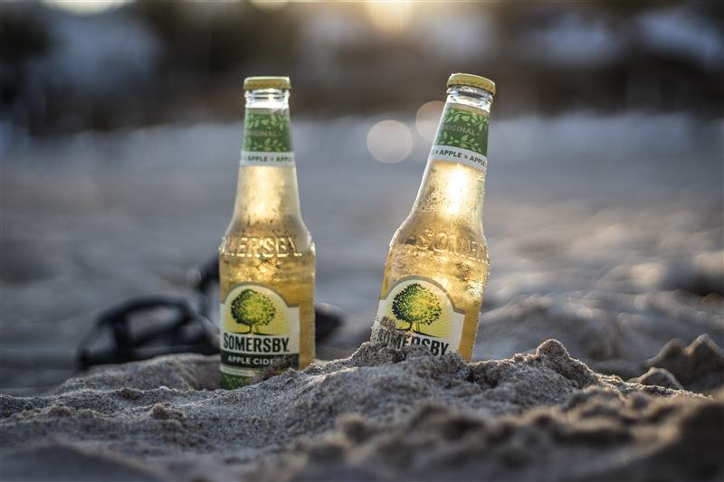 Apple cider bottles on the beach in summer evening with sunset